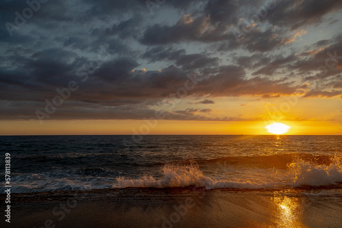 Sea storm on a sunset. Wave comes to a shore in front of vivid sunset at golden hour