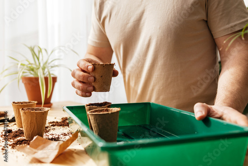 A close -up man putting peat cups in a home greenhouse. Growing vegetables and herbs at home. Landscaping of the apartment.