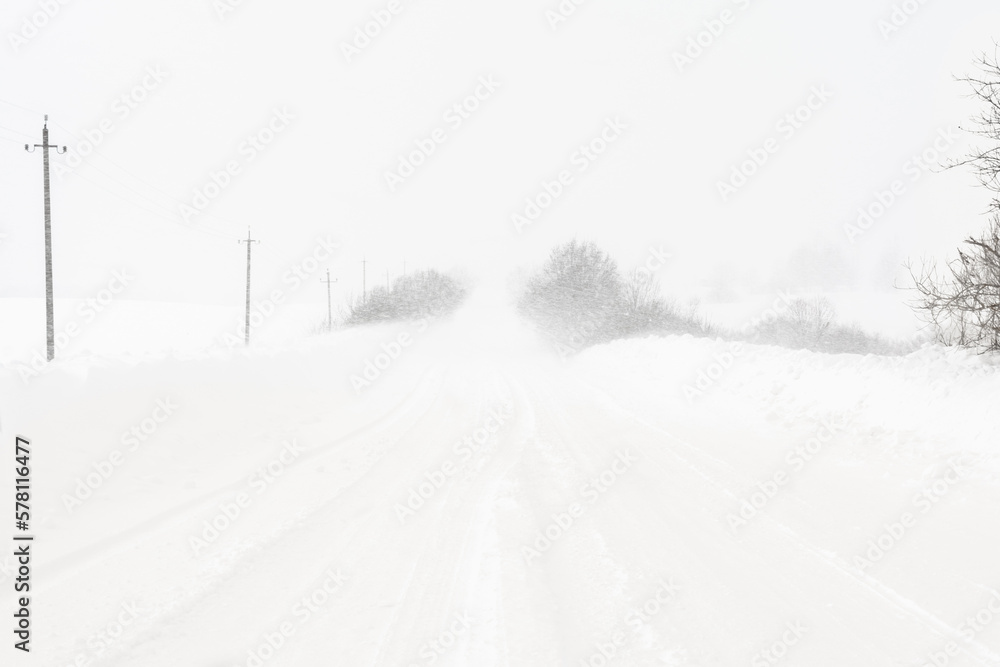 A heavy snowstorm covers the road. Large snowdrifts on the sides of a rural road. Poor visibility during a snow cyclone