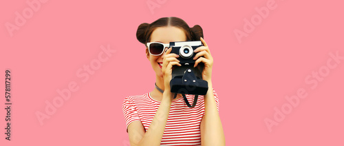 Portrait of happy young woman photographer with film camera, female with cool girly hairstyle on pink background © rohappy