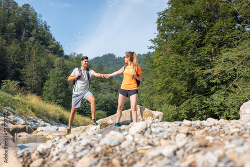 Young couple, walking along the rocky shore of a mountain river, exploring beautiful nature. Concept of an active vacation.