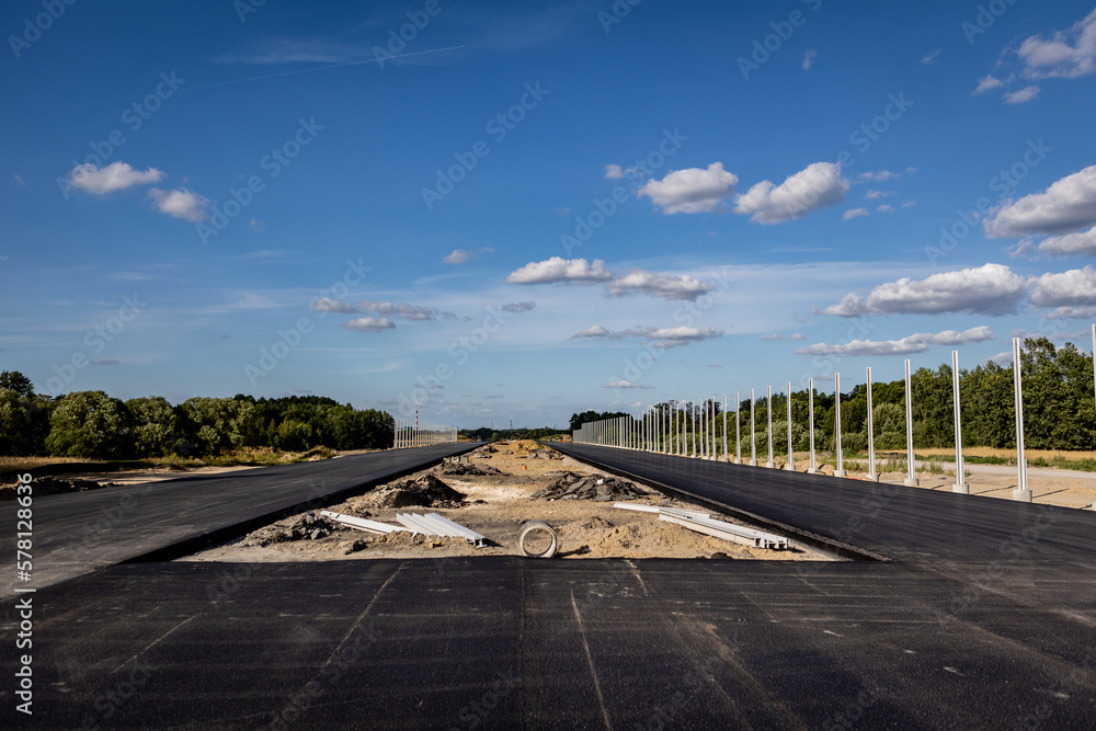 Budowa nowej autostrady. Montaż barier ochronnych i znaków przy nowo budowanej autostradzie. Nowy asfalt. - obrazy, fototapety, plakaty 