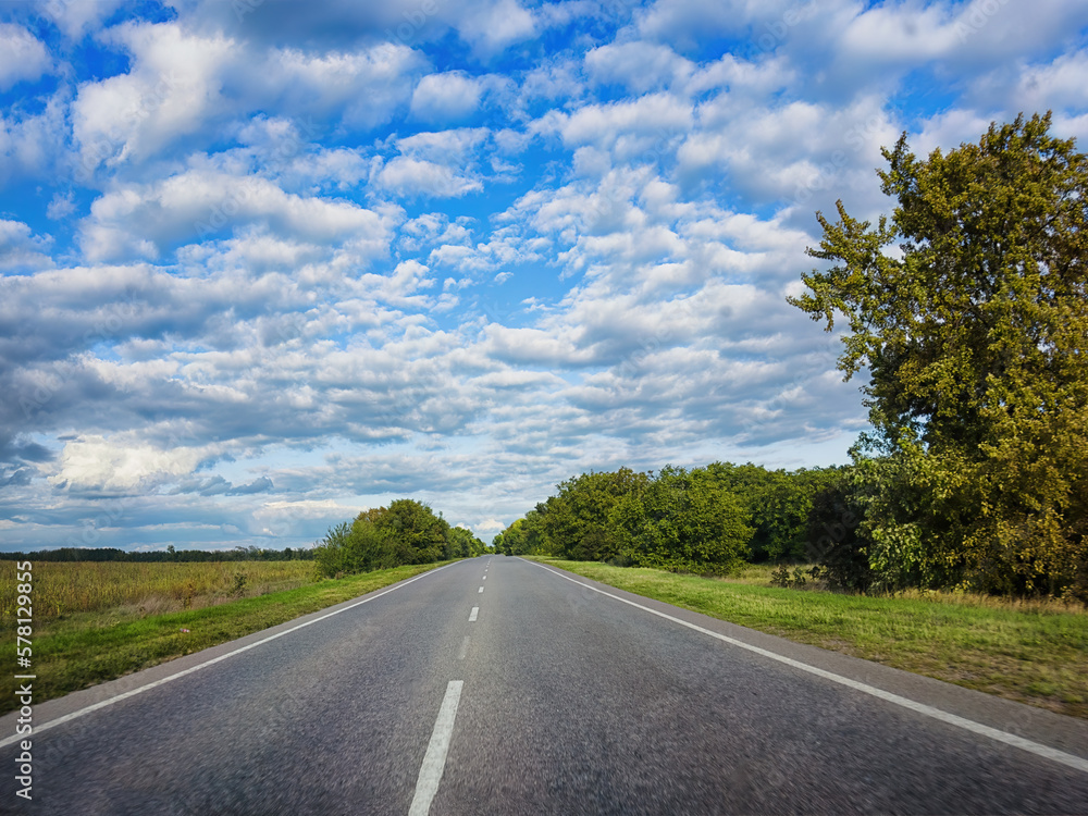 Summer empty road, highway. Green trees, fields, white clouds and blue sky