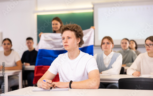 Female teacher tells her classmates about the country of Russian, holding a flag in her hands