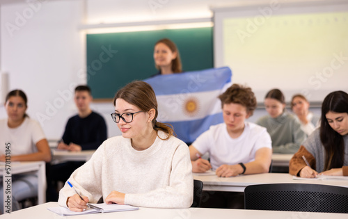 Geography lesson in school class - teacher talks about Argentina  holding a flag in his hands