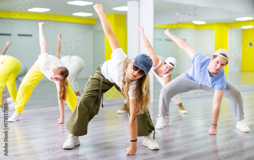 Active teenage girl practicing breakdance go downs in training hall. Teenagers engaged in breakdance in dance studio