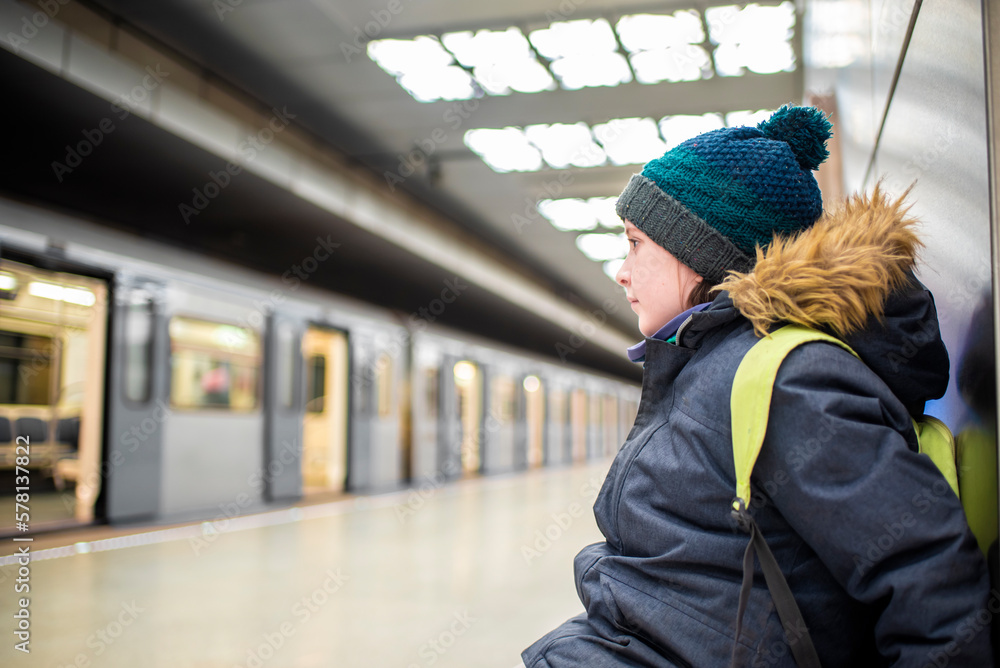 a smiling boy in a winter jacket and hat is waiting for an approaching train on a subway platform a smiling boy in a winter jacket and hat is waiting for an approaching train on a subway platform