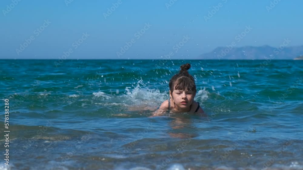 Child try to swim in waves on beach. A view of smiling sporty little girl swimming and have fun in the sunny sea water. A concept of luxury summer trips during vacation. Child try to swim in waves on beach. A view of smiling sporty little girl swimming and have fun in the sunny sea water. A concept of luxury summer trips during vacation.