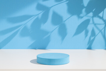 Pastel blue podium for products or cosmetics against bright blue background with leaves shadows.	
