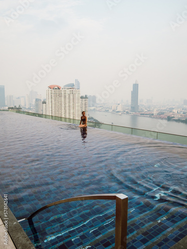 Caucasian woman is sitting at an infinity pool on a rooftop in Bangkok, Thailand