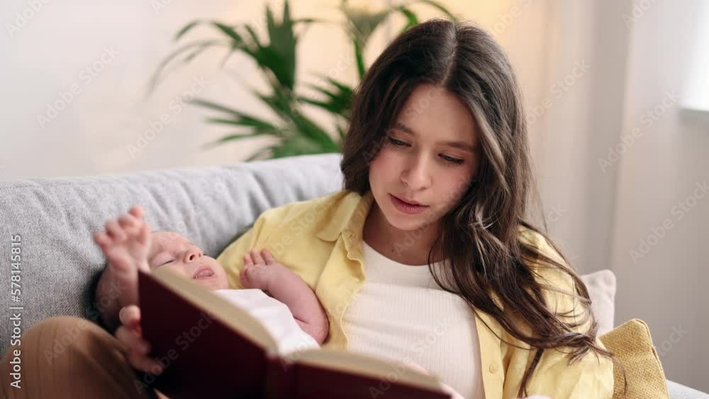 Portrait of cute young family spend leisure time together when mother reading book literature to her little baby soothes the child with his pleasant voice laying on sofa at light room Portrait of cute young family spend leisure time together when mother reading book literature to her little baby soothes the child with his pleasant voice laying on sofa at light room