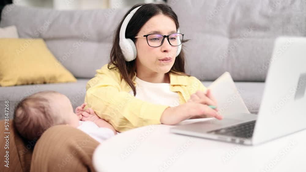 Portrait of busy young business mother holding her baby while working or studying on laptop computer and make notes at light home office Successful woman balancing work or education and motherhood