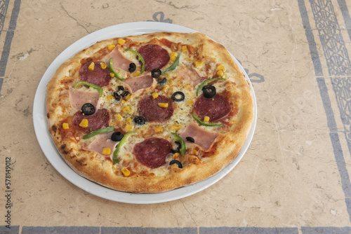 A pepperoni pizza with peppers, ham and sweetcorn with black olives prepared in a kebab restaurant