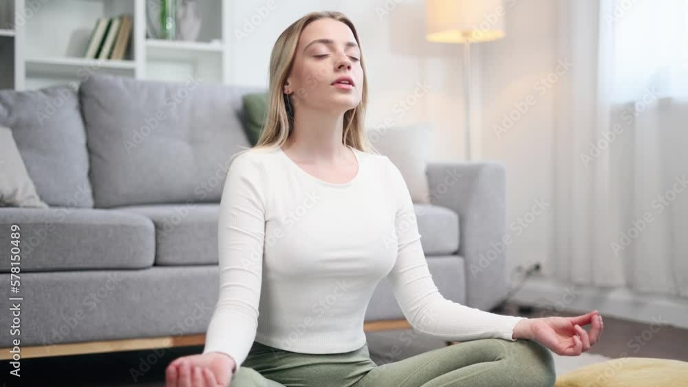 Close up portrait of calm relaxed young blond woman keeps hands in yoga gesture meditating and breathes slowly while make asanas in light living room at home No stress happy people concept Close up portrait of calm relaxed young blond woman keeps hands in yoga gesture meditating and breathes slowly while make asanas in light living room at home No stress happy people concept