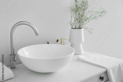Sink and vase with flowers on table in light bathroom