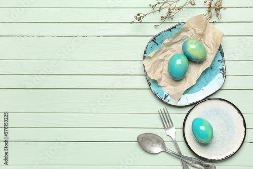 Table setting with Easter eggs, cutlery and floral decor on green wooden background
