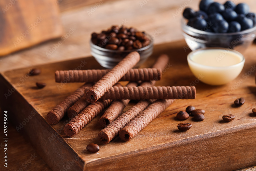 Board with delicious chocolate wafer rolls, condensed milk and blueberries on brown wooden table