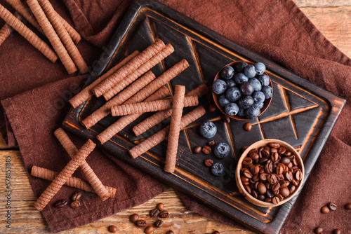 Board with delicious chocolate wafer rolls, blueberries and coffee beans on brown wooden table