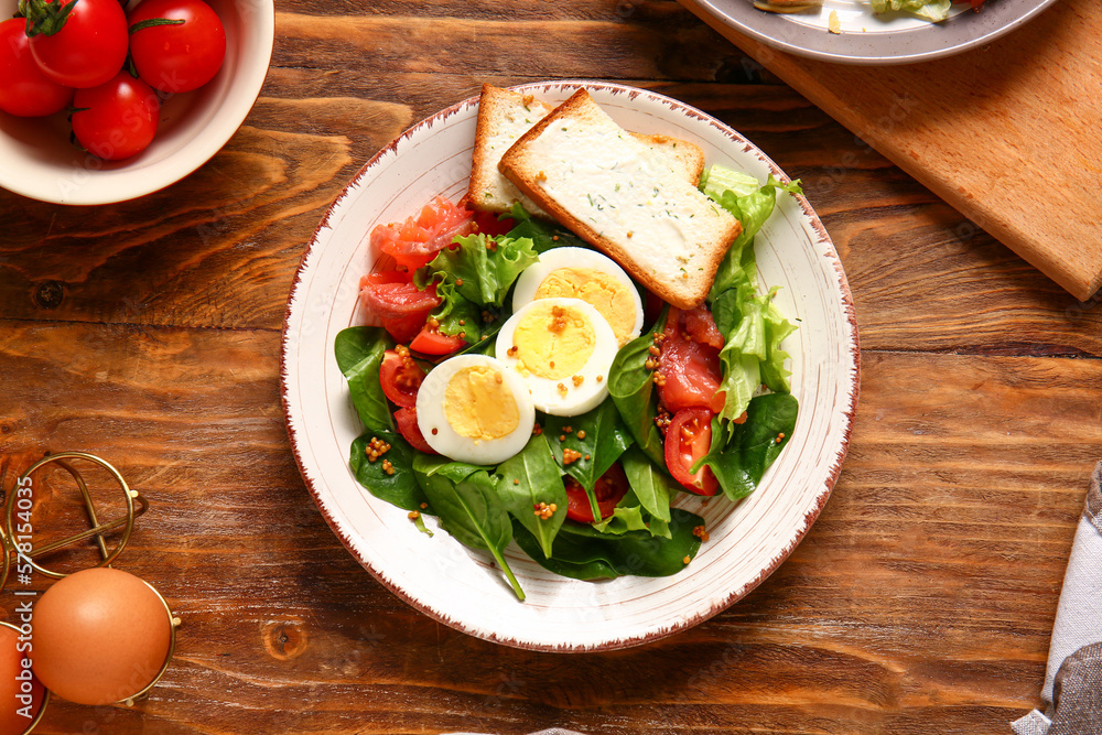 Plate of delicious salad with boiled eggs and salmon on brown wooden background