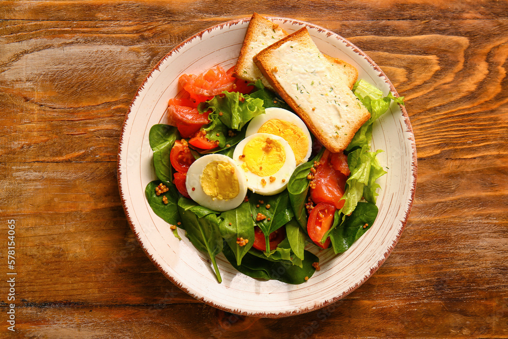 Plate of delicious salad with boiled eggs and salmon on brown wooden background Plate of delicious salad with boiled eggs and salmon on brown wooden background