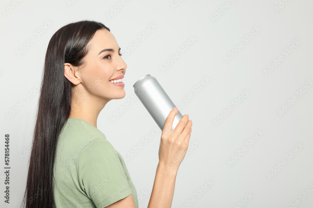 Beautiful happy woman holding beverage can on light grey background. Space for text Beautiful happy woman holding beverage can on light grey background. Space for text