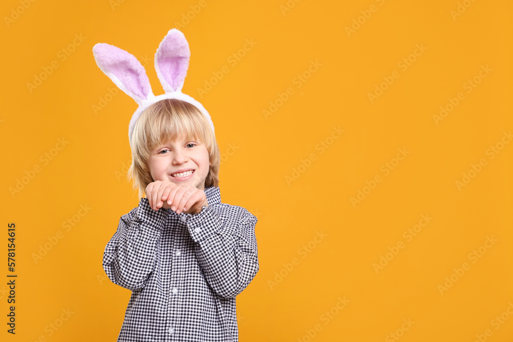 Happy boy wearing bunny ears headband on orange background, space for text. Easter celebration Happy boy wearing bunny ears headband on orange background, space for text. Easter celebration