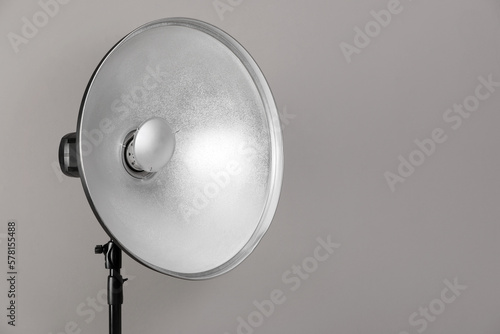 Professional beauty dish reflector on tripod against grey background, space for text. Photography equipment © New Africa