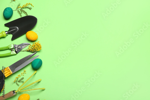 Gardener's tools with Easter eggs and flowers on green background