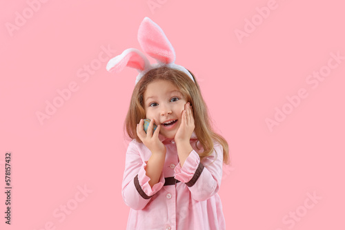 Cute little girl in bunny ears with Easter egg on pink background