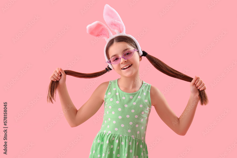 Cute little girl in bunny ears and sunglasses on pink background