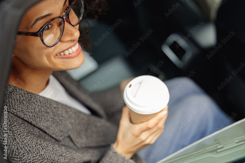 Poster Print Smiling woman passenger in eyeglasses drinking takeaway coffee in taxi car on th 40x26.7 cm