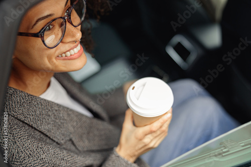 Fototapete Smiling woman passenger in eyeglasses drinking takeaway coffee in taxi car on th