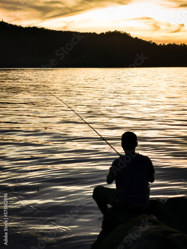 Outdoor scenery during sunset with silhouette of a fisherman fishing.