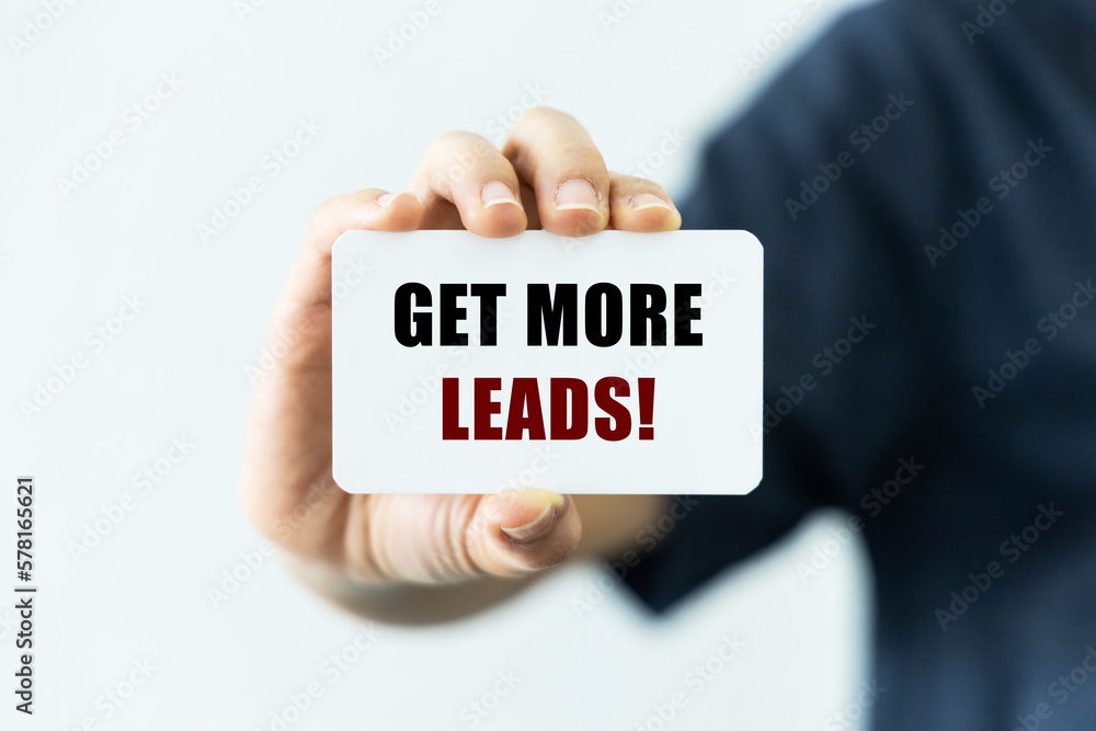 Get more leads text on blank business card being held by a woman's hand with blurred background. Business concept about getting more leads. Get more leads text on blank business card being held by a woman's hand with blurred background. Business concept about getting more leads.