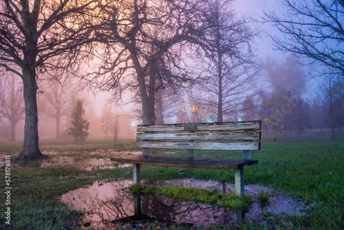 Peaceful park with a park bench for relaxing, on a beautiful and colorful misty morning during sunrise. Nature is a perfect place for solitude to clear the mind and calm the soul. 