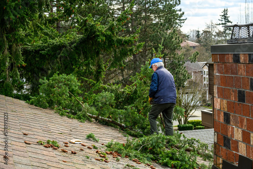 Senior man throwing a large fir tree branch and storm other debris off a residential rooftop 