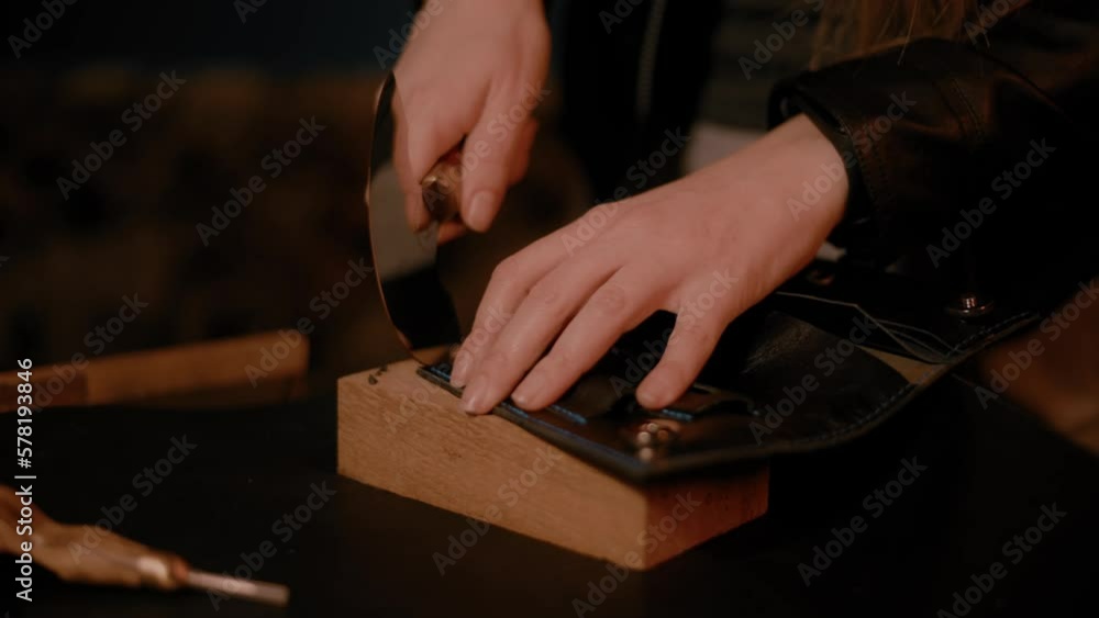 Woman hands using a round head knife, cutting leather in the workshop, dark setup, high contrast, color graded Woman hands using a round head knife, cutting leather in the workshop, dark setup, high contrast, color graded