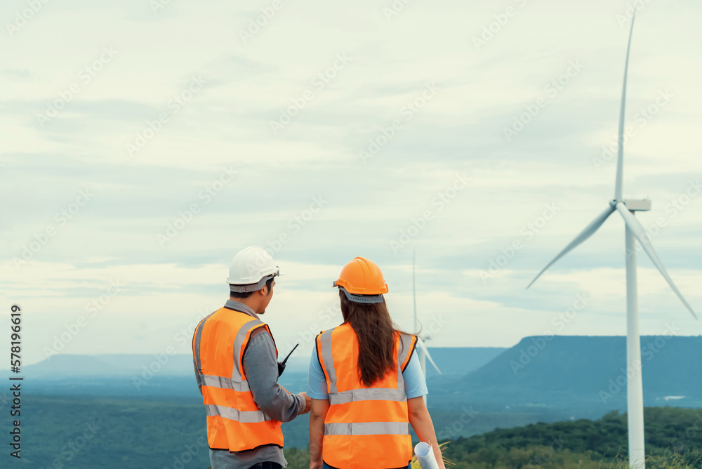Male and female engineers working on a wind farm atop a hill or mountain in the rural. Progressive ideal for the future production of renewable, sustainable energy. - obrazy, fototapety, plakaty 