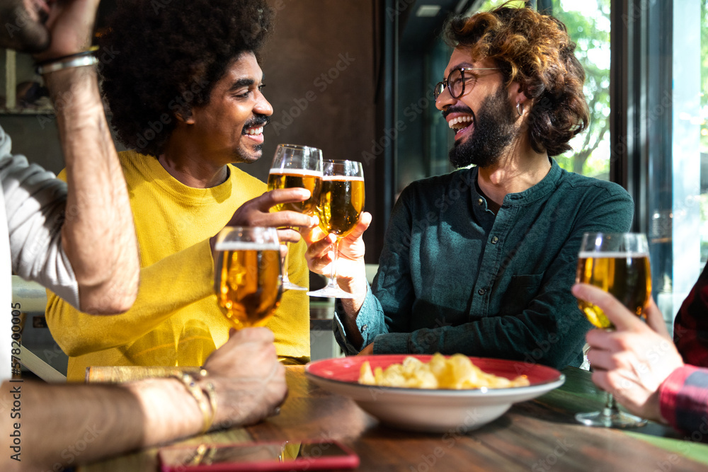 Vertical portrait of happy multiracial male friends in a bar looking at camera toasting with beer.