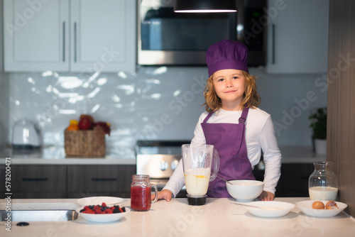 Child 7-8 years old in chef hat and apron. Kid chef cook wearing uniform cook cap and apron cooked food in the kitchen.