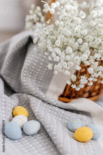 A wicker brown basket, inside which, on a gray linen napkin, are painted yellow, blue, white eggs and white small flowers. Spring background for Easter. Mock up. Space for text