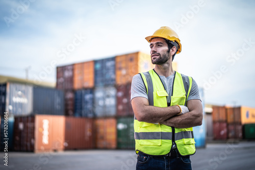 Caucasian warehouse worker in uniform with hard hat standing in container port terminal. Area logistics import export and shipping.