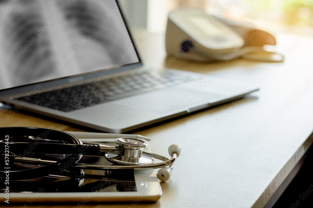 Doctor's office desk with medical stethoscope, laptop computer, digital tablet, electronic pen and sphygmomanometer on wooden table at office. Doctor's office desk with medical stethoscope, laptop computer, digital tablet, electronic pen and sphygmomanometer on wooden table at office.