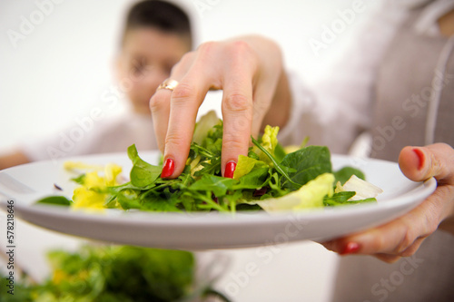 cooking salad mom with hand adds lettuce leaves to large bowl in background boy stirs salad kitchen cooking aprons cooking homemade food communication children helping child in cooking training