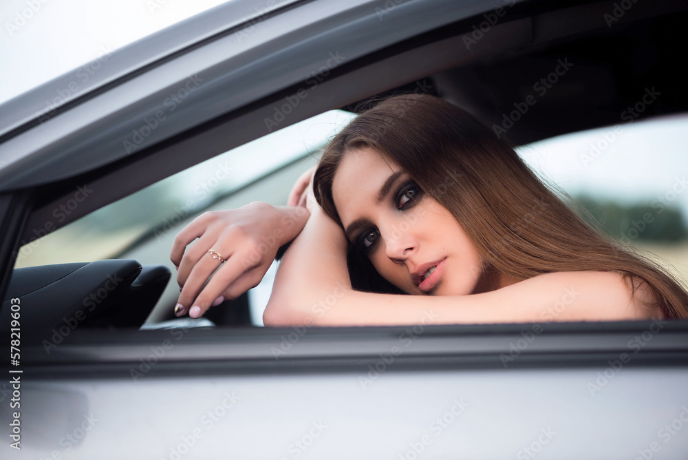 Beautiful young girl sits in the car seat on the empty road.