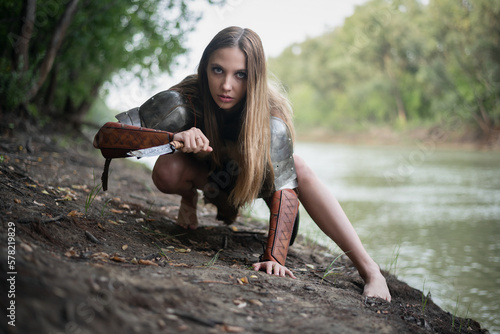 Bild auf Leinwand Beautiful girl warrior with the knife is hunting on the river shore