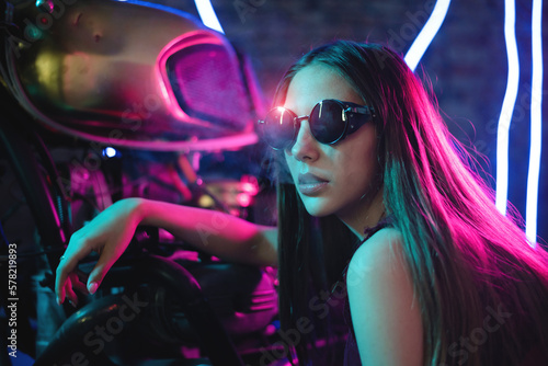 Girl a motorbiker near the cyberpunk motorcycle in the neon lights.