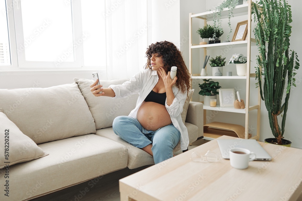 Pregnant woman smile blogger showing baby feeding bottle filming herself on phone, video chat sitting on sofa at home freelancer in last month of pregnancy lifestyle before childbirth Pregnant woman smile blogger showing baby feeding bottle filming herself on phone, video chat sitting on sofa at home freelancer in last month of pregnancy lifestyle before childbirth