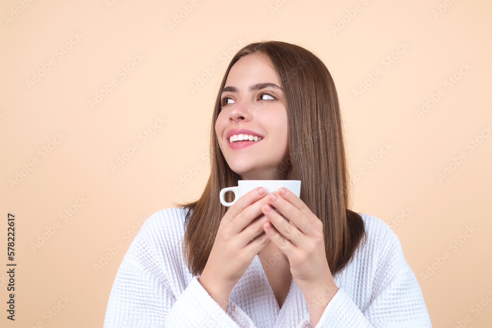 Morning coffee. Close up portrait of happy young woman with cup of coffee. Smiling girl drinking coffee isolated on beige studio background. Pretty woman in bathrobe with cup of hot coffee. Morning coffee. Close up portrait of happy young woman with cup of coffee. Smiling girl drinking coffee isolated on beige studio background. Pretty woman in bathrobe with cup of hot coffee.