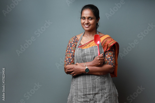 Indian ethic woman wearing apron and holding spatula showing a like gesture photo